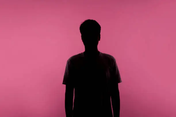 Photo of Anonymous person. Silhouette portrait of young man in casual T-shirt isolated on pink background
