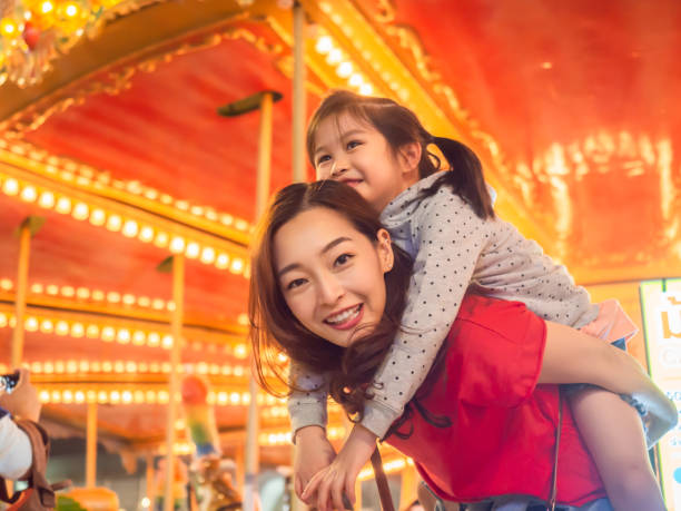 felice asia madre e figlia divertirsi nel parco di carnevale divertimento con ruota farris e sfondo carosello - ferris wheel immagine foto e immagini stock