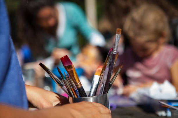 istock Kid is holding a metal container full of paintbrushes while sitting outside 1197211674