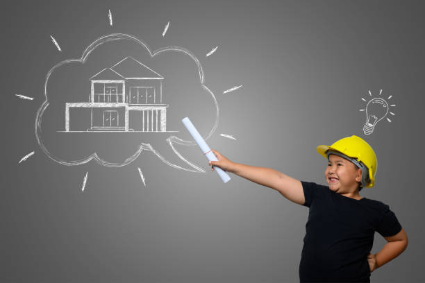 istock A boy wearing a yellow engineer hat and a house plan on a blackboard 1197220520