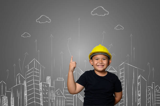 istock A boy wearing a yellow engineer hat and a house plan on a blackboard 1197220525