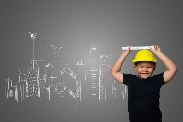 istock A boy wearing a yellow engineer hat and a house plan on a blackboard 1197220564