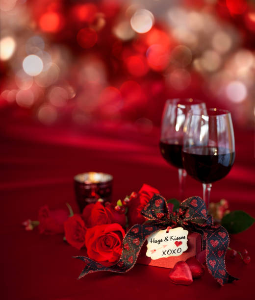 Romantic candlelight dinner on red background.  Valentine's dinner scene includes: wine, candles, plate, rose petals and heart gift box.  No people.