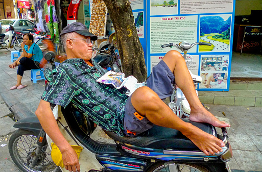 Hanoi, Vietnam; October 13 2013.  Man sleeping on a motorbike on street in the Old Quarter.
