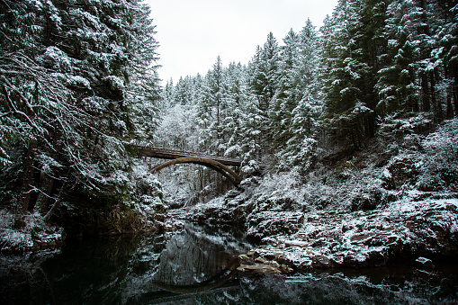 A beautiful Pacific Northwest scene - a iconic bridge standing 75 feet above a crystal clear river during the winter snow scene. This footbridge is found in the state of Washington.