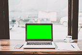 Mockup image of laptop with blank green screen on wooden table of In the coffee shop.