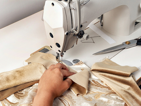 Female hands at work on a sewing machine. Seamstress sews curtain elements. Scissors, pins, close up, side view