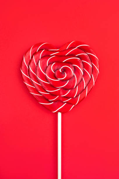 una piruleta en forma de corazón sobre un fondo rojo. concepto del día de san valentín. - flavored ice lollipop candy affectionate fotografías e imágenes de stock