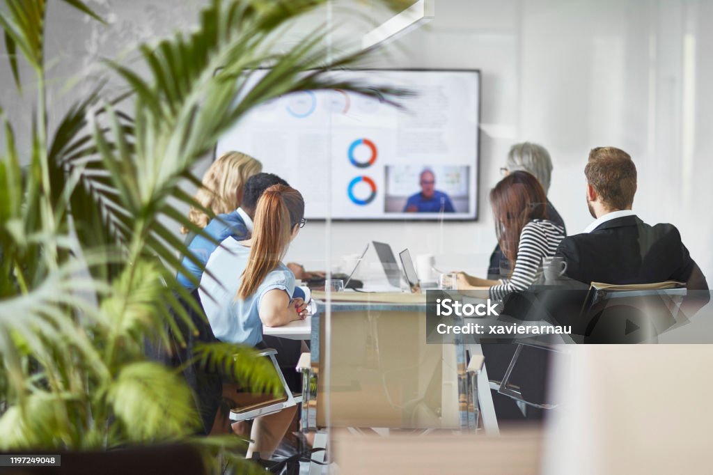 Male and Female Executive Team Video Conferencing with CEO Rear view photographed through window of diverse male and female executive team video conferencing with CEO in office board room. Office Stock Photo
