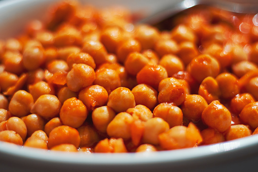 Close-up of spoon and chickpea dish with tomato sauce on plate