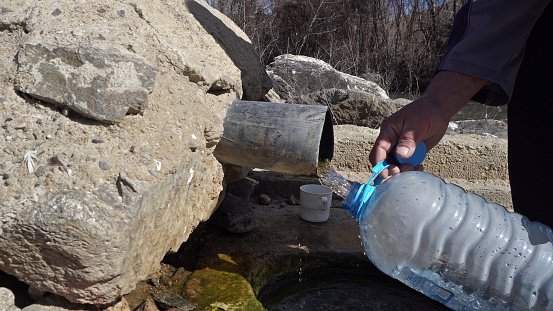 Old man fill plastic bottle with thermal drink water from natural spring