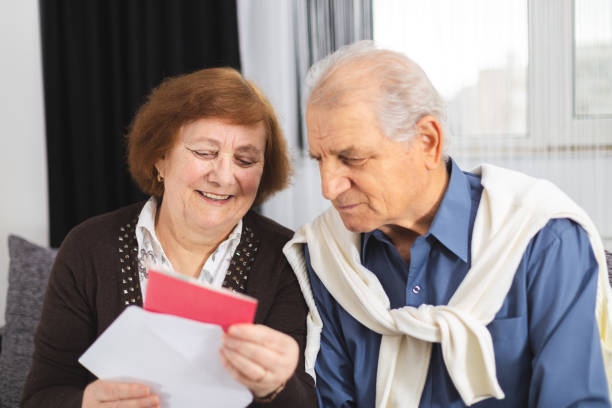 Senior couple standing on the couch and reading a letter received. Portrait Of A Happy Senior Couple At Home Reading Paper stock photo
