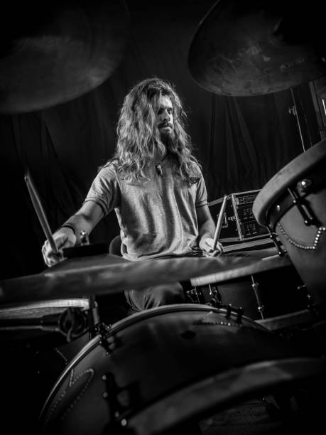 Young man playing the drums on stage Young long-haired drummer playing his drum set during a concert. drum kit photos stock pictures, royalty-free photos & images