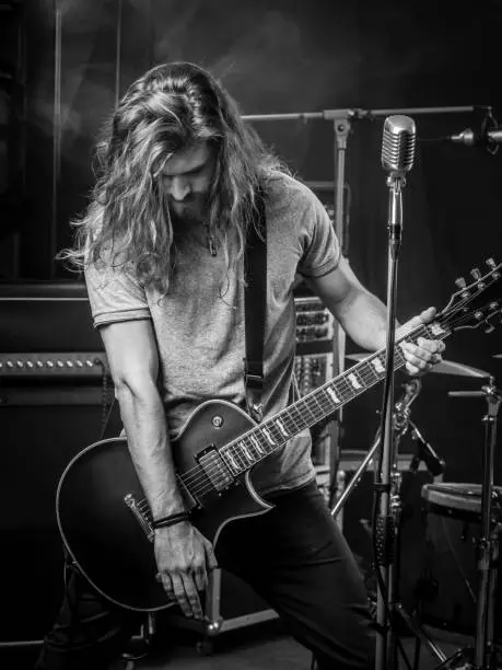 Photo of a young man with long hair playing electric guitar on stage.