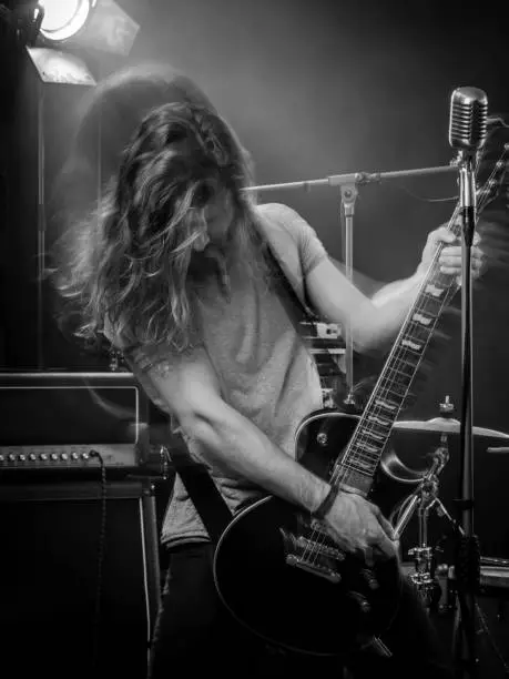 Photo of a young man playing electric guitar on stage and tossing his long hair around. Blurred motion with double exposure.
