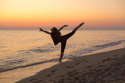 Silhouette of an energetic girl dancing ballet on the beach at sunset
