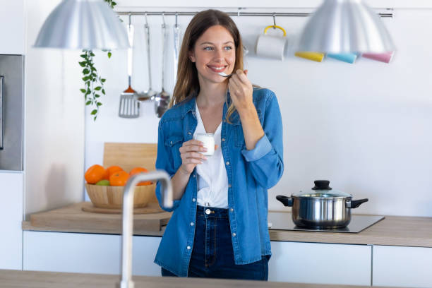 istock Pretty young woman eating yogurt while standing in the kitchen at home. 1197263128