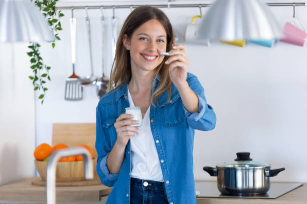 istock Pretty young woman looking at camera while eating yogurt in the kitchen at home. 1197263200