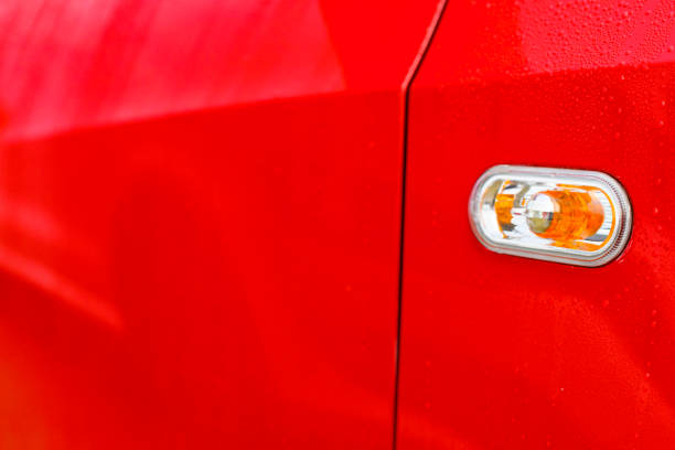 Detail on a modern compact suv car in bright red. The lines of the car are emphasized by the soft outdoor light and the raindrops on the car's surface.