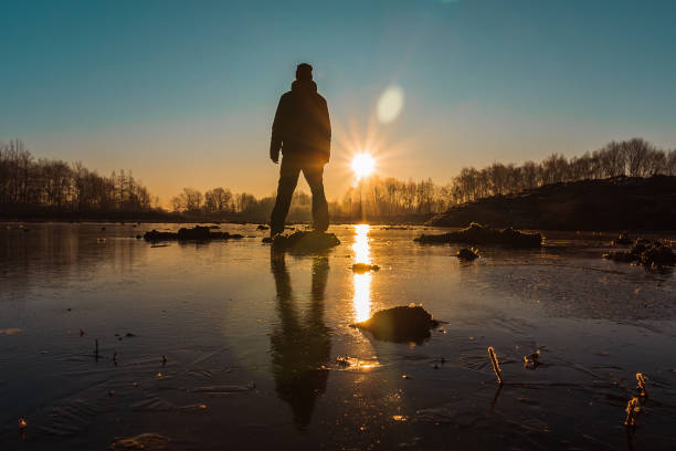 istock Young man from back standing on ice in pond with sun and trees 1197265651