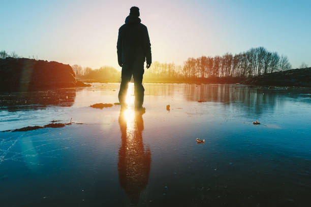 istock Young man standing on ice in pond with sun and trees 1197265673
