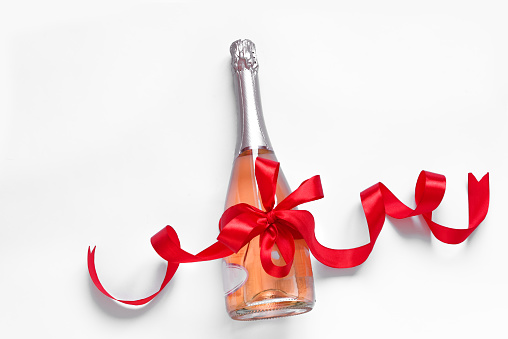 Champagne bottle with red bow ribbon on white background, copy space. Celebration holiday concept.