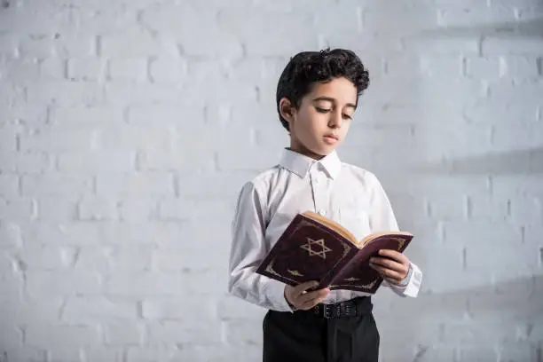 Photo of cute jewish boy in white shirt reading tanakh