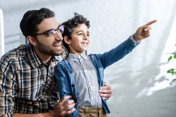 smiling jewish son pointing with finger and looking through window with father in apartment smiling jewish son pointing with finger and looking through window with father in apartment yarmulke photos stock pictures, royalty-free photos & images