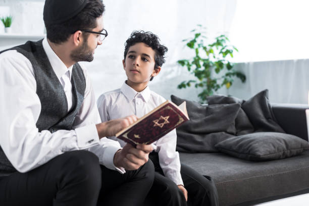 padre judío e hijo hablando y sosteniendo tanakh en apartamento - judaísmo fotos fotografías e imágenes de stock