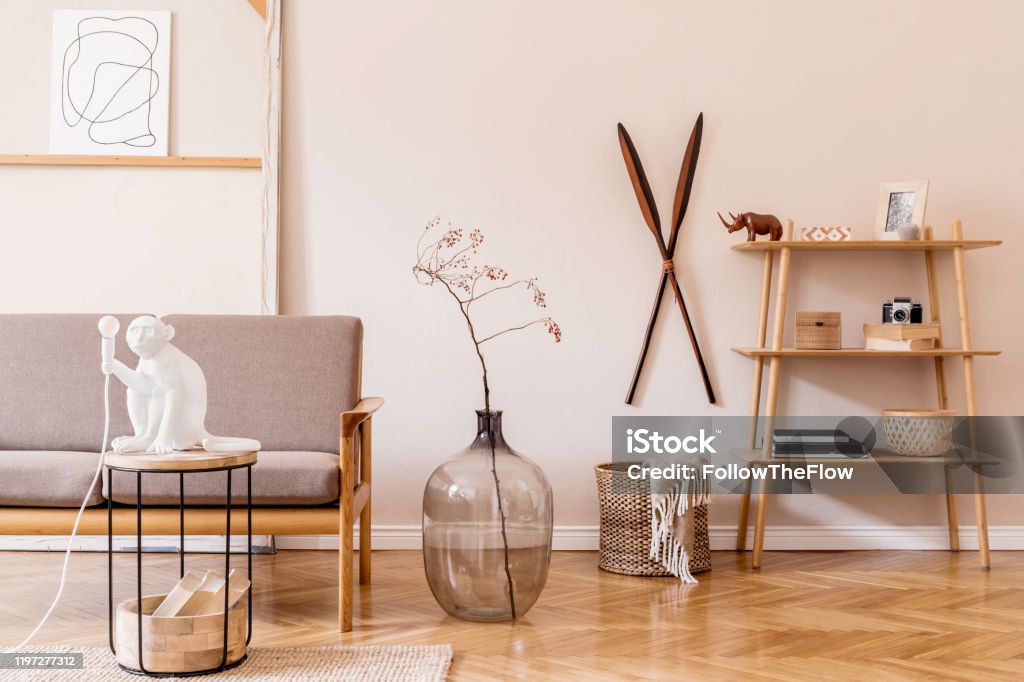 Stylish interior design of living room at cozy apartment with brown sofa, coffee table with lamp, bookstand, vase and elegant accessories. Minimalistic concept of home staging Beige wall. Template. Stylish interior of living room. Beige and japandi concept. Modern home staging. Template. Japandi Stock Photo