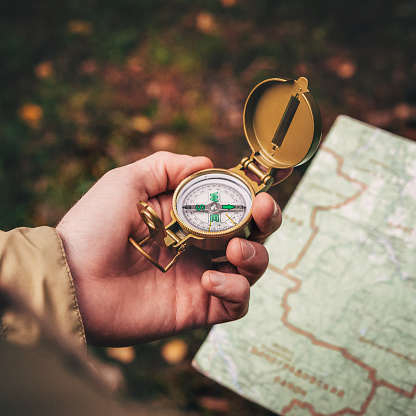 A man holds a compass and a paper map in his hand and is guided by the area, autumn forest, walk,hiking