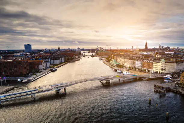 HDR image of Copenhagen cityscape with modern bicycle bridge, contemporary office buildings and residental flats at the up class oceanfront, Nyhavn, shot with drone. Dramatic cloudscape and lens flare in background.