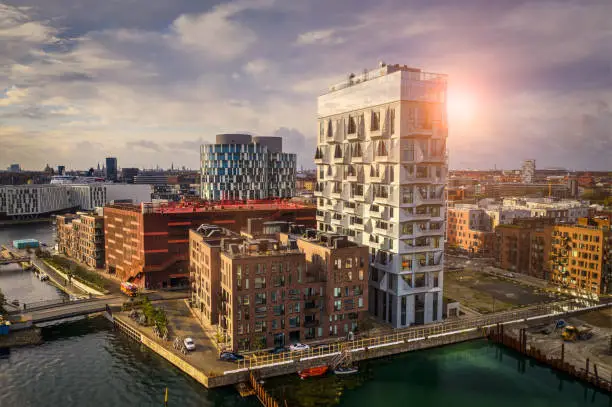 HDR image of Copenhagen cityscape with contemporary office buildings and residental flats at the up class oceanfront, Nordhavn, shot with drone. Dramatic cloudscape and lens flare in background.