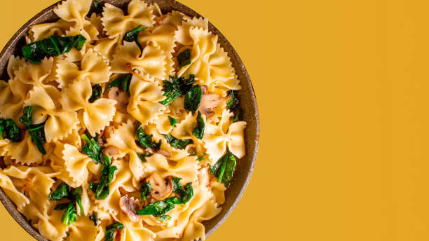 istock butterfly pasta with fried mushrooms, green spinach in a pan on an orange background. copy space 1197292511