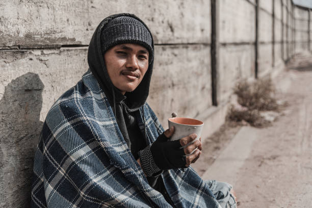 un homme s'asseyant contre un bâtiment de brique avec sa tête dans ses bras - brick wall homelessness wall begging photos et images de collection