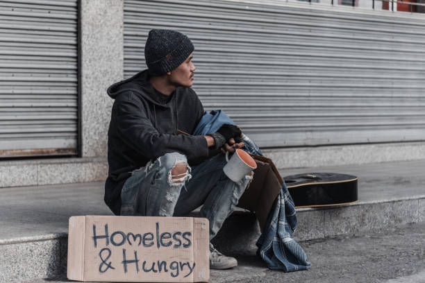 un homme s'asseyant contre un bâtiment de brique avec sa tête dans ses bras - brick wall homelessness wall begging photos et images de collection