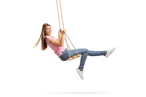 Full length shot of a young woman with long hair swinging on a wooden swing isolated on white background