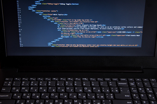 Source code or HTML code on screen of laptop, keyboard. Close up css code on monitor screen with black background, binary code on dark background