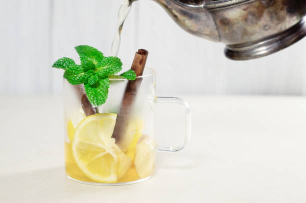istock Pouring hot tea from a teapot into a cup with lemon, cinnamon and mint 1197309979