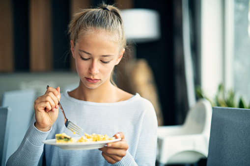 Teenage girl having breakfast. The girl is holding a plate with scrambled egg.\nNikon D850