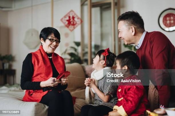 Cute Little Granddaughter And Grandson Dressed In Red Traditional Chinese Costume Greeting To Grandparents And Receives Red Envelops Joyfully In Chinese New Year Stock Photo - Download Image Now