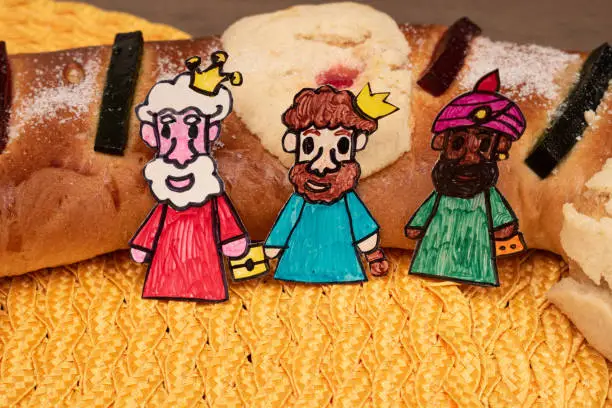 Three wisemen made of cardboard and traditional Epiphany cake on yellow background