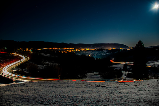 beautiful night panorama of the Asiago plateau, Veneto, Italy. Headlights trails of cars in the curves of the snowy road