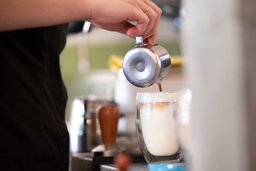 Close up on hands of a barista preparing a milk coffee with the espresso machine in the background.