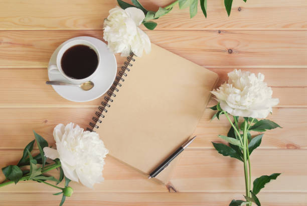 istock Morning coffee cup for breakfast, empty notebook and white peony flowers on wooden table. 1197338657