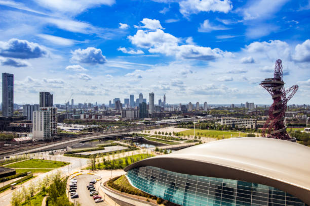 london aquatics centre mit canary wharf am horizont an einem sonnigen tag und unter blauem himmel mit weißen wolken. - the bigger picture englische redewendung stock-fotos und bilder