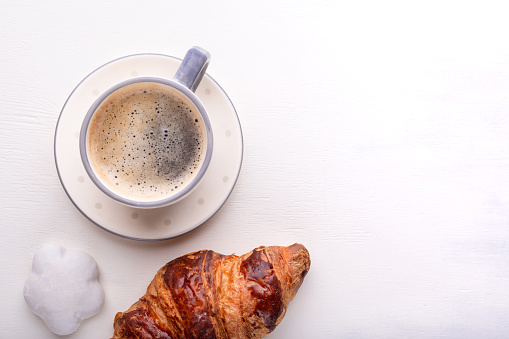 Croissants, glazed cookies and a cup of coffee on a white wooden table. Morning still life. Top view with space for text. Flat lay composition. Background for restaurant, bakery, cafe.