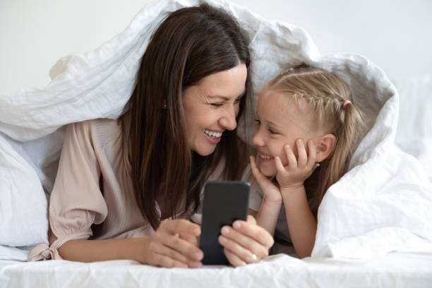 istock Happy mother lying under blanket with daughter, using smartphone. 1197373145