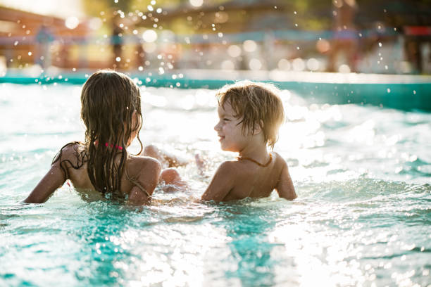 istock Rear view small boy sitting in pool and splashing 1197376030