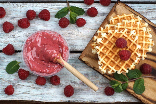 Pink whipped honey in a jar with a spindle spoon, juicy large raspberries and sweet waffles on the table, top view